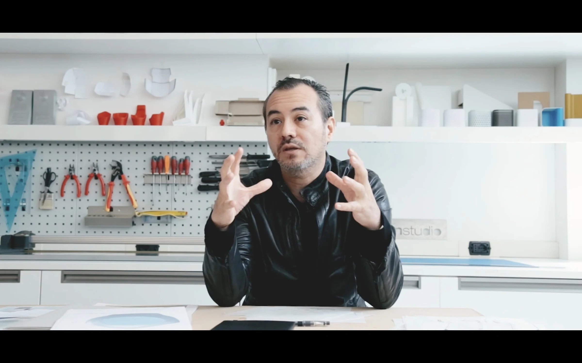 A designer explaining his process at a workbench in a product studio