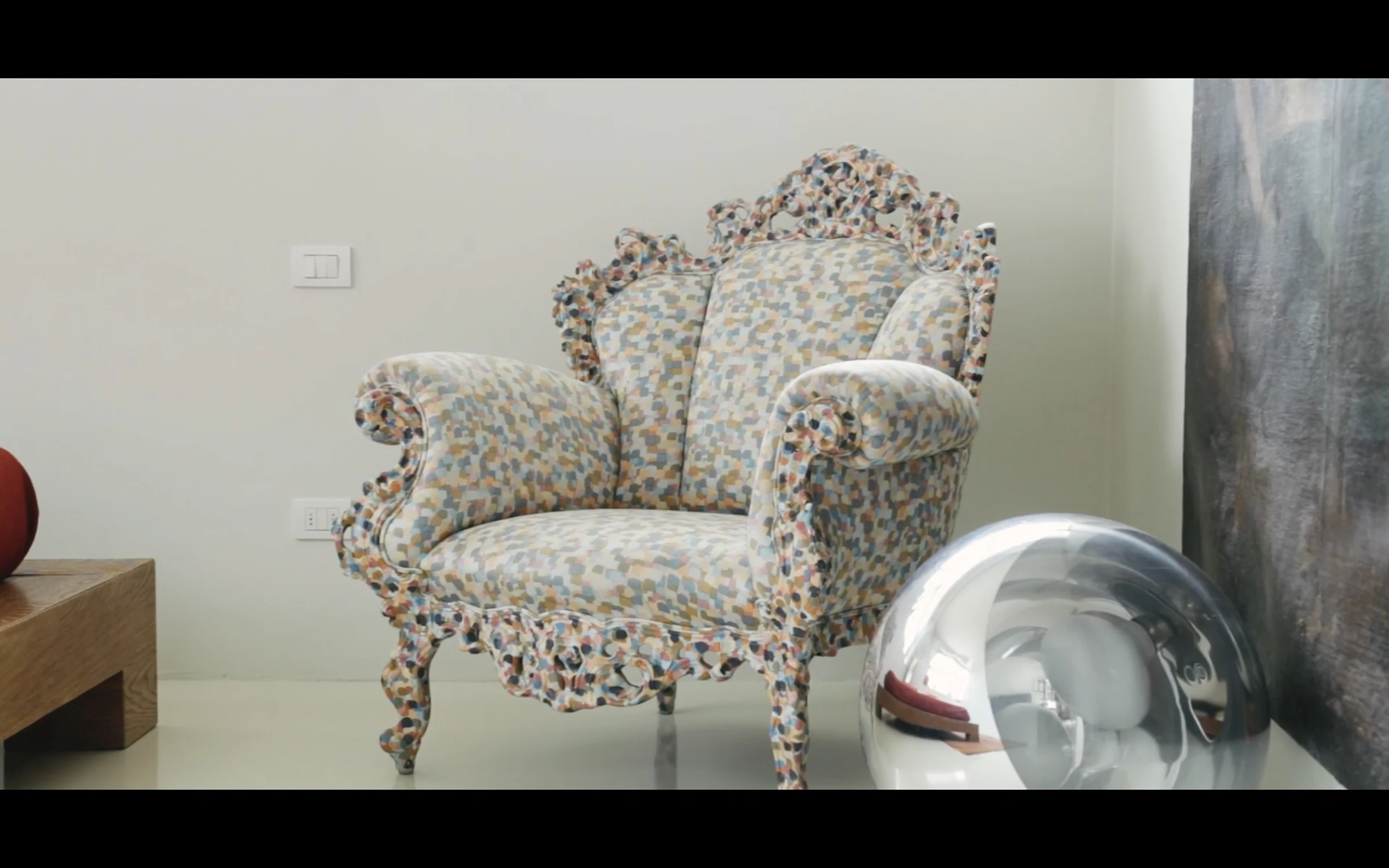 A floral-patterned armchair beside a mirrored sphere in a gallery setting
