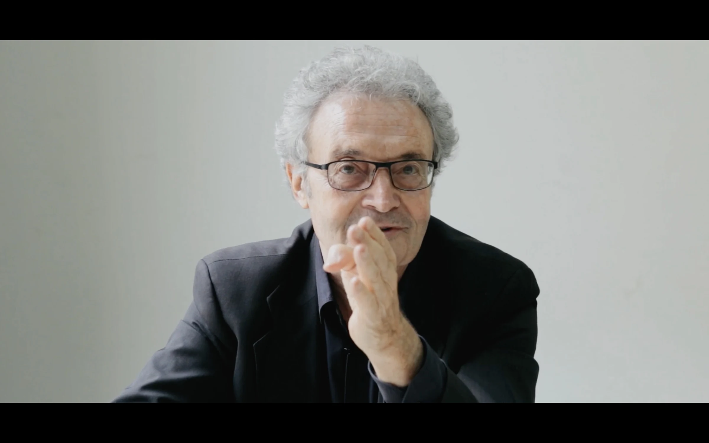 An older Italian designer resting his chin on his hand, listening
