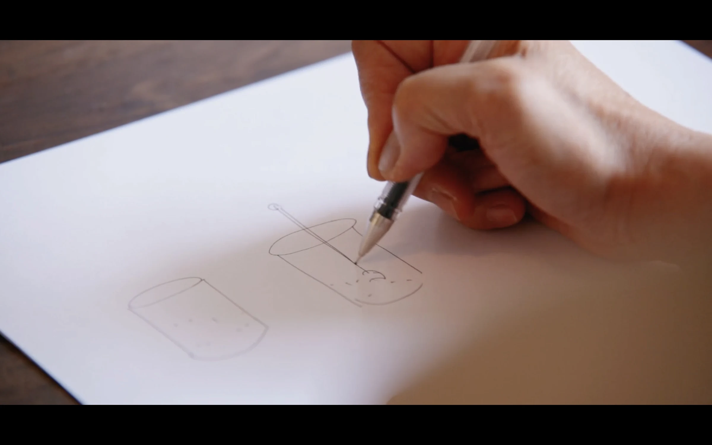 A hand drawing a geometric outline in pencil on paper