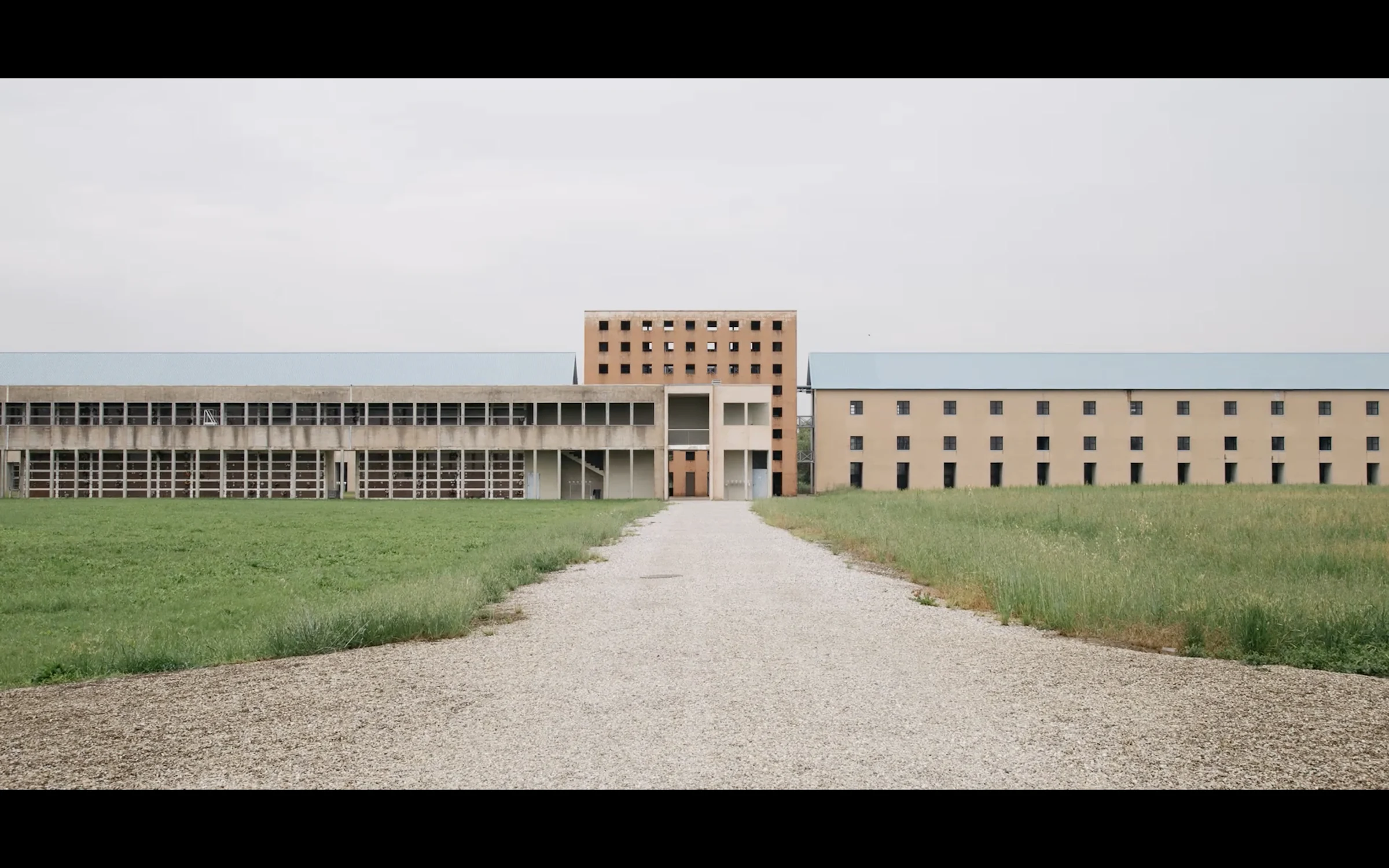 A long modernist building at the end of a gravel path under a pale sky